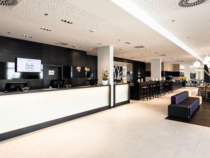 Moderna recepción de hotel con mostrador largo, área de asientos y decoración de pared iluminada.