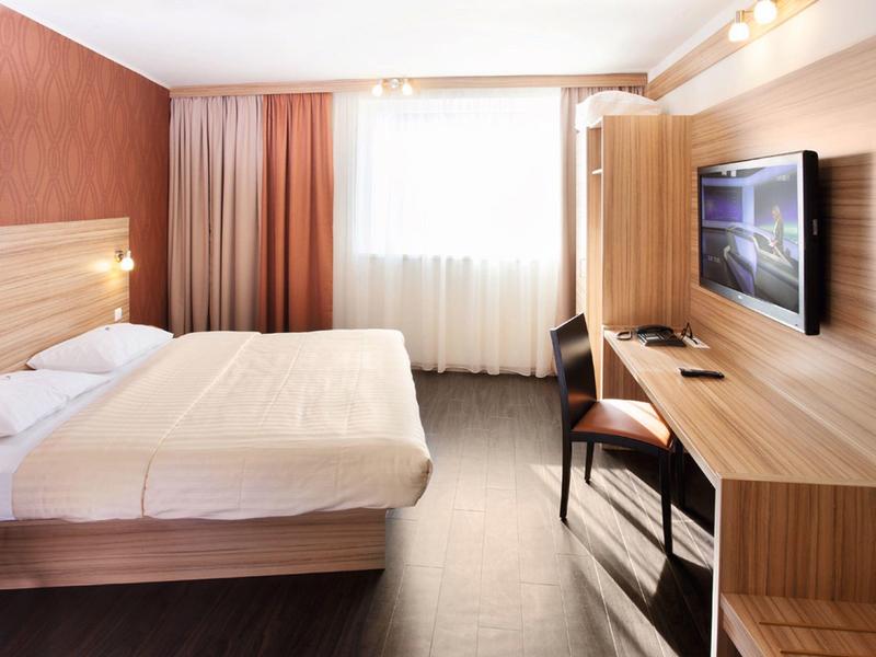 Modern hotel room with large bed, desk, and wall-mounted TV.