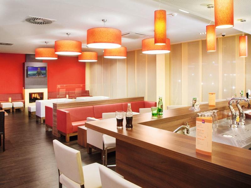 Modern hotel bar and dining area with orange ceiling lamps and white seating.