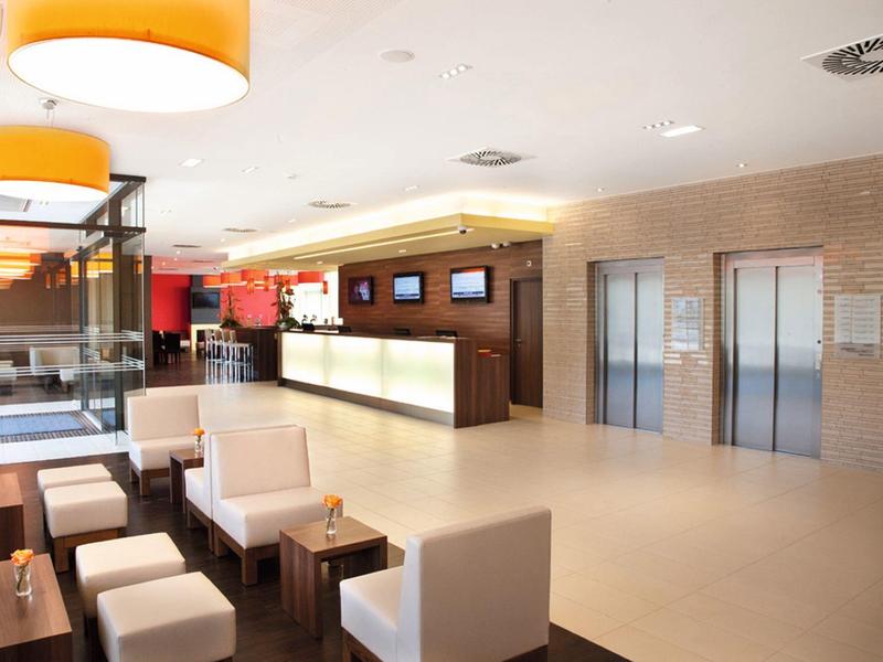 Modern hotel lobby with reception, seating area, and elevators under warm lighting.