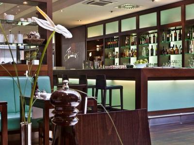 Moderne Bar mit Holztheke, beleuchteten Regalen, Blumenarrangement und Barhockern.