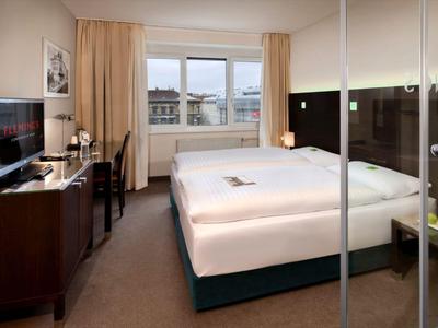 Modern hotel room with double bed, desk, flat-screen TV, and window view.
