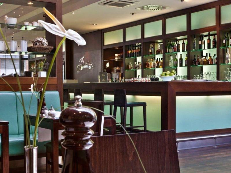 Bar moderne avec tabourets hauts, étagères éclairées remplies de bouteilles et fleurs décoratives.