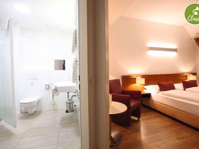 Moderní hotelový pokoj s manželskou postelí a přilehlou koupelnou se sprchou.