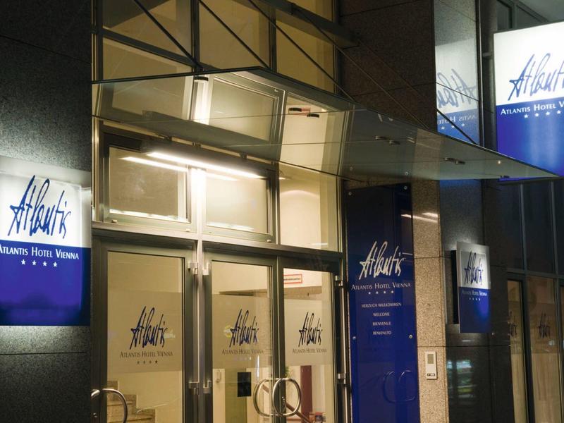 Hotelentree met verlichte borden en moderne glazen luifel in de nacht.