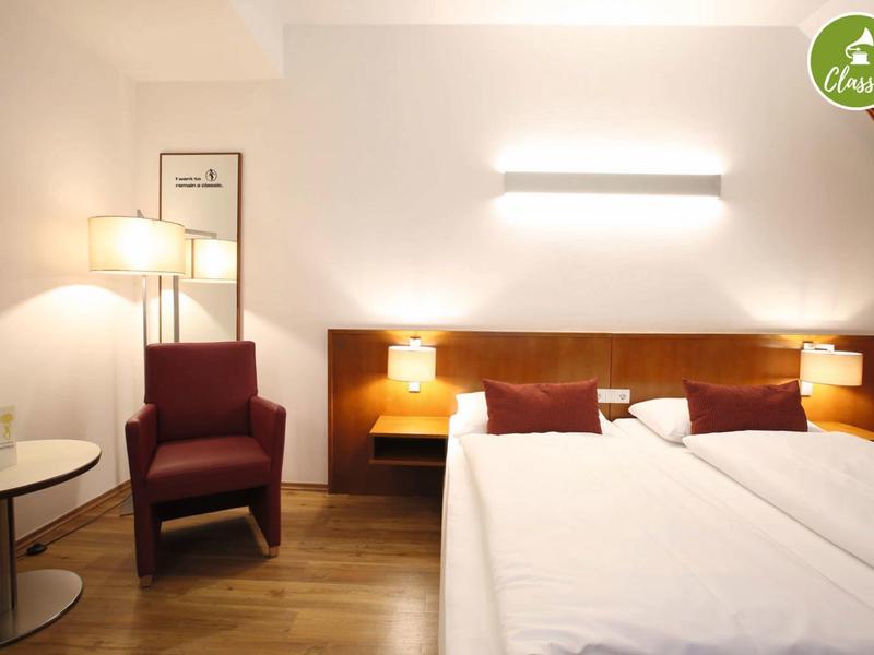 Modern ingerichte hotelkamer met twee bedden, een fauteuil en zachte verlichting.