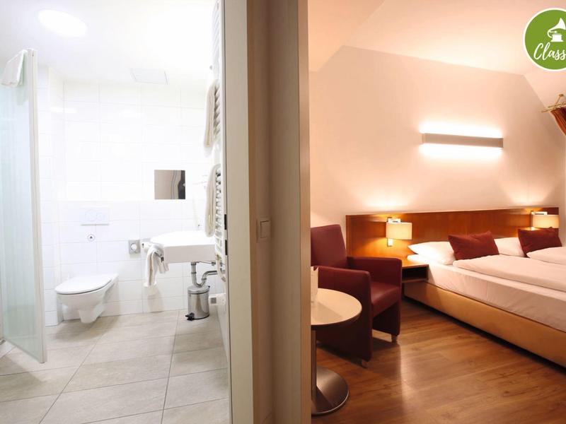 Verlicht hotelkamer met tweepersoonsbed en aangrenzende moderne badkamer.