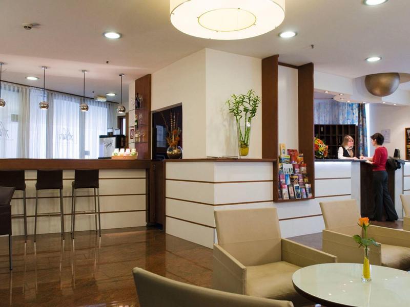 Moderne hotellobby met receptiebalie, barkrukken en zithoek.
