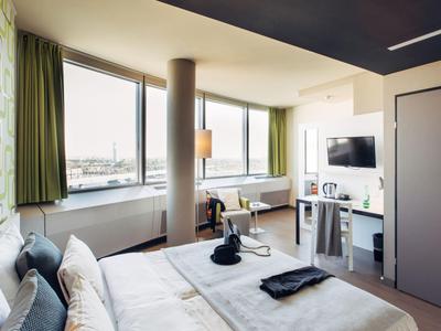 Habitación de hotel moderna con ventana grande, cama doble y televisor.