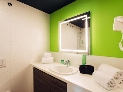 Baño moderno con pared verde, espejo iluminado y lavabo.
