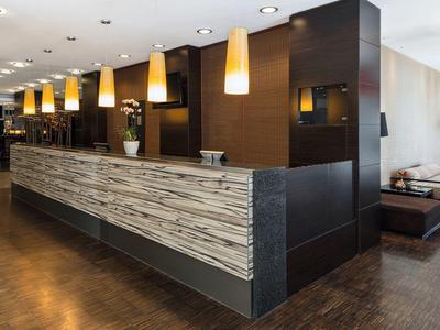 Moderne Hotellobby mit langem Tresen, Holzverkleidung und warmem Licht von Hängelampen.