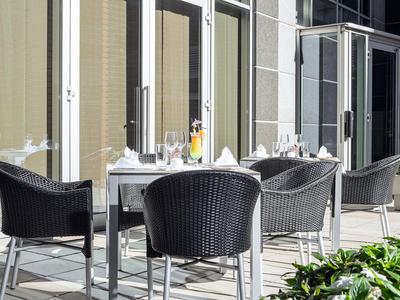 Venkovní jídelní prostor s moderními černými proutěnými židlemi a prostřenými stoly