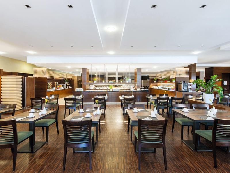 Moderner, heller Gastraum mit Holzboden, mehreren Tischen und Stühlen, eleganter Buffettheke im Hintergrund.