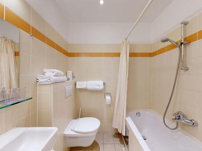 Lichte badkamer met bad, toilet, wastafel en oranje tegelaccenten.