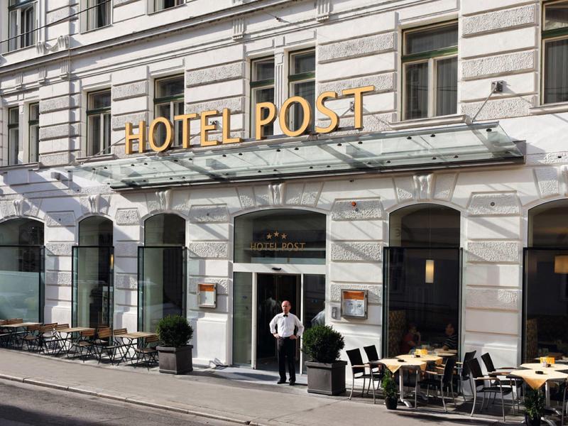 Fasada hotelu z miejscami do siedzenia na zewnątrz i napisem HOTEL POST dużymi złotymi literami.