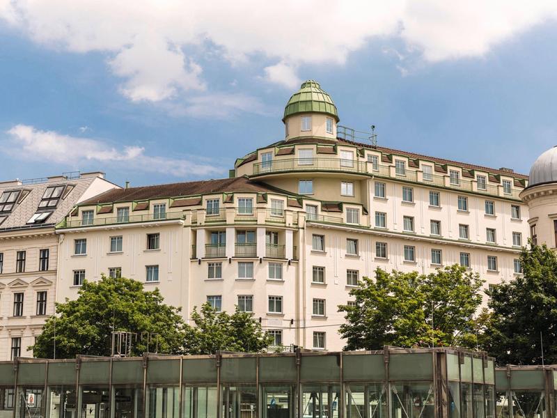 Historická budova hotelu s kupolí a balkóny pod zamračenou oblohou.