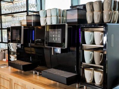 Coffee machines on a wooden counter with stacked cups in a café or hotel.