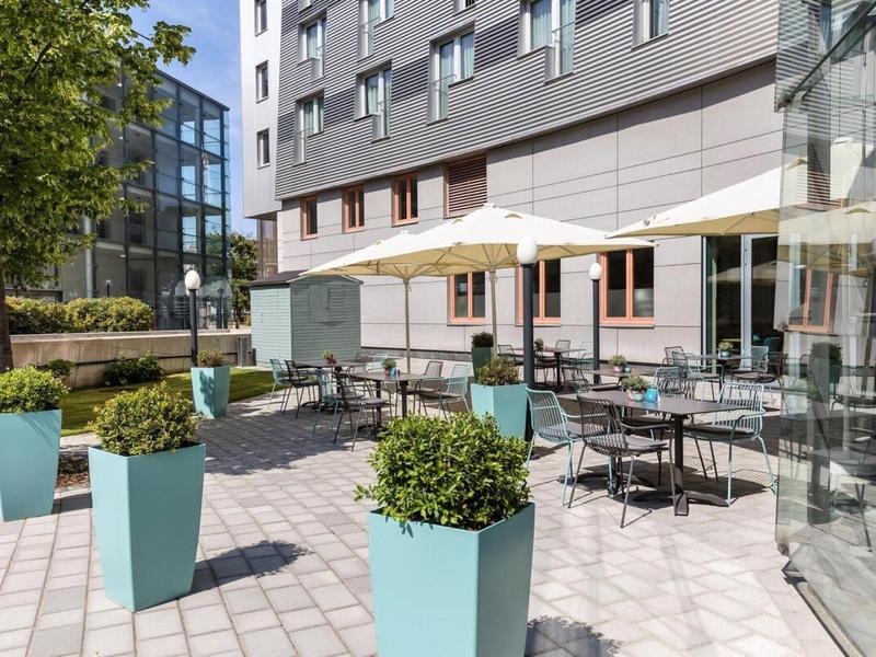 Modern outdoor hotel area with tables, chairs, and umbrellas on the terrace.