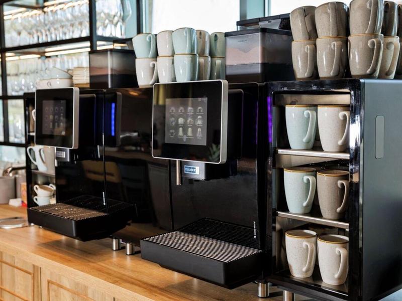 Modern coffee machines with several stacked white cups on a wooden counter.