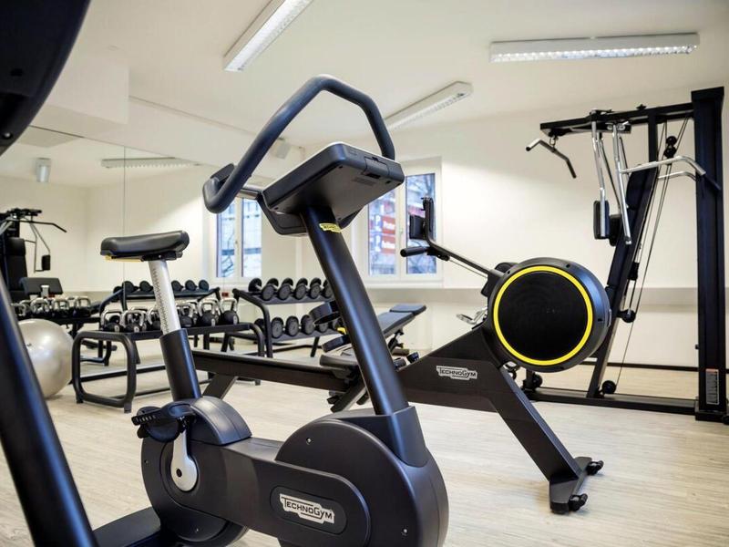 Modern gym with exercise bike, dumbbells, and strength training machine in bright room.