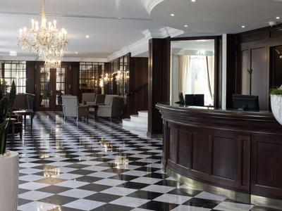 Elegante hotellobby met marmeren tegelvloer en donkere houten inrichting.