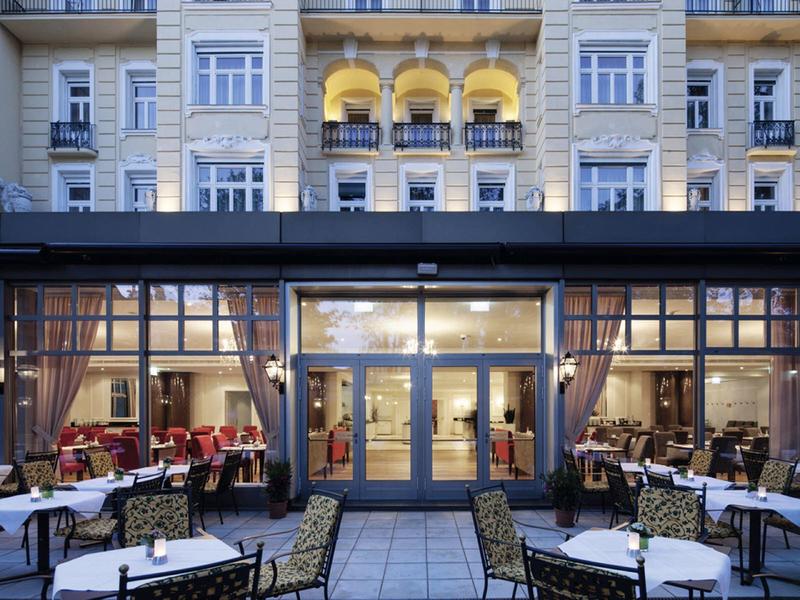 Elegantní venkovní jídelní prostor hotelu s prostřenými stolky před historickou budovou.