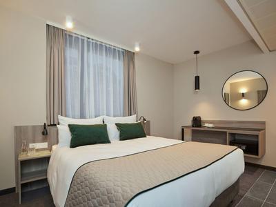 Modern hotel room with large bed, gray bedspread, and green pillows.