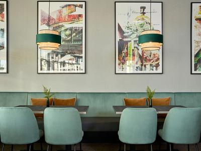 Moderní posezení s pastelově modrými židlemi, zelenými rostlinami a barevnými obrazy na stěně v restauraci.