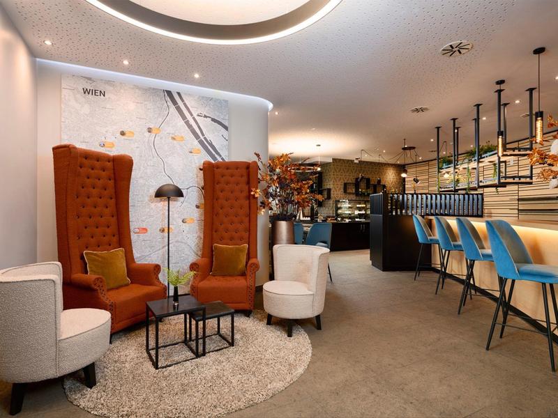 Cozy hotel lounge with armchairs, rug, and bar featuring blue stools and decorations.