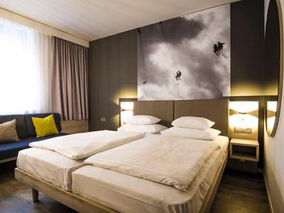 Modernes Schlafzimmer mit zwei Einzelbetten, grauer Wand, großem Fenster und gemütlicher Couch.