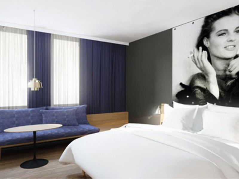 Chambre d'hôtel moderne avec grand lit, canapé bleu et grand portrait en noir et blanc sur le mur.