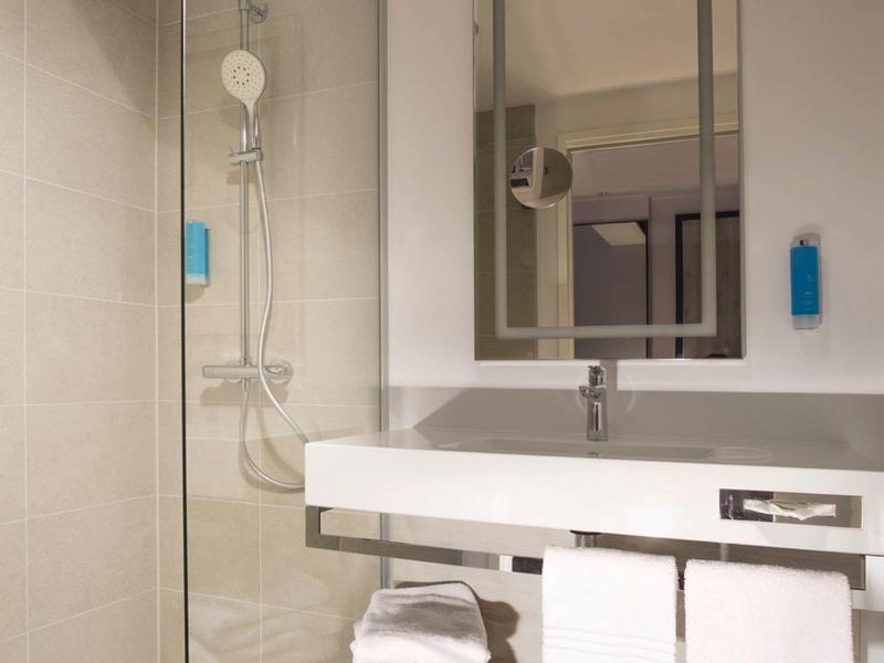 Salle de bain d'hôtel moderne avec douche en verre, lavabo blanc et serviettes.