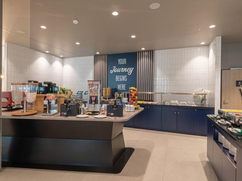 Lounge dell'hotel moderna con buffet self-service e selezione di caffè in ambiente luminoso.