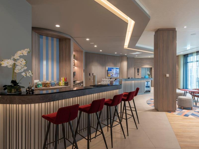 Area bar moderna in hotel con sgabelli rossi e interni in legno chiaro.