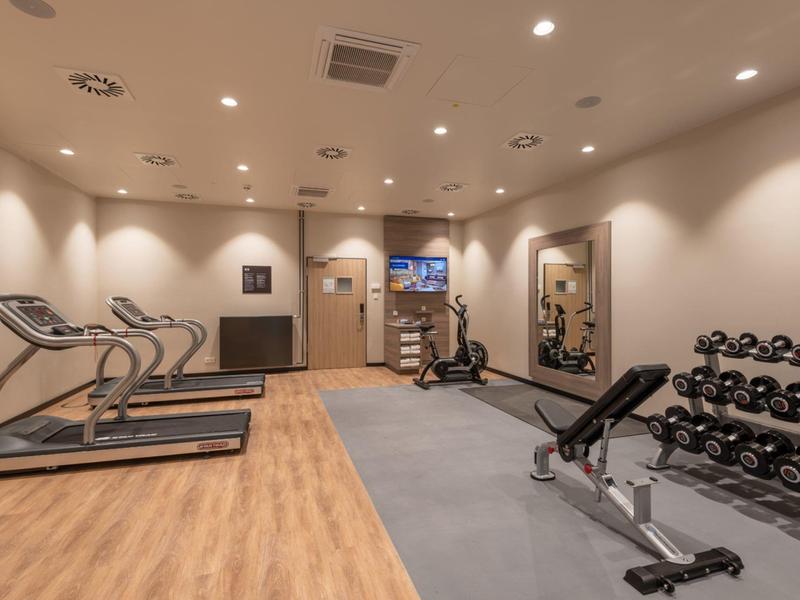 Palestra moderna con tapis roulant, pesi e panca in ambiente luminoso.