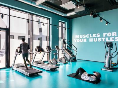 Modern gym with large windows, exercise machines, and a person relaxing on a mat.