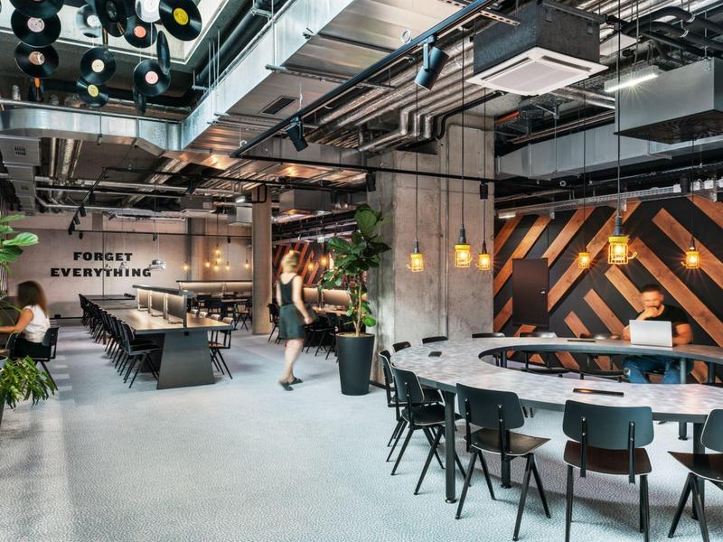 Moderní hotelová lobby s odpočinkovou zónou, stoly, židlemi a elegantním industriálním designem.