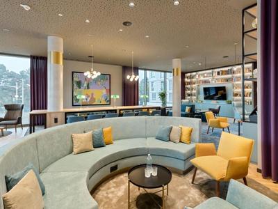 Moderne Lounge mit gebogener grauer Couch, gelben Sesseln und großem Fenster mit Blick.