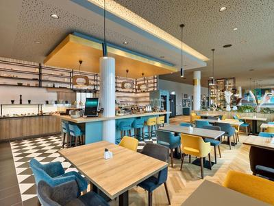 Modernes Restaurant mit Holztischen, blauen Stühlen und Deckenleuchten in einem Hotel.