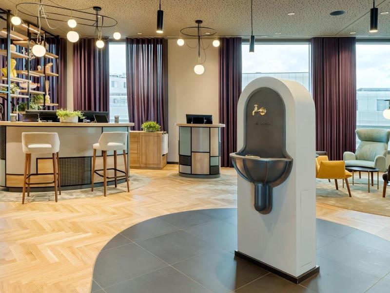 Lobby moderna de hotel con barra, suelo de madera y dispensador de desinfectante en el centro.