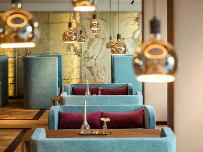 Modern hotel bar with turquoise booths, golden hanging lamps, and wooden tables.