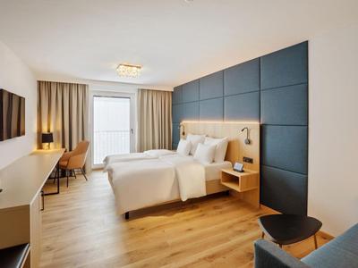 Modern hotel room with double bed, blue wall panels, desk, and wall-mounted TV.