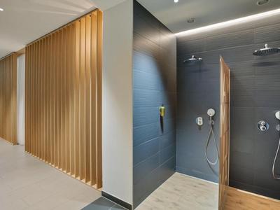 Moderní, elegantní sprchový prostor s béžovými dřevěnými panely a tmavými dlaždicemi v hotelové koupelně.