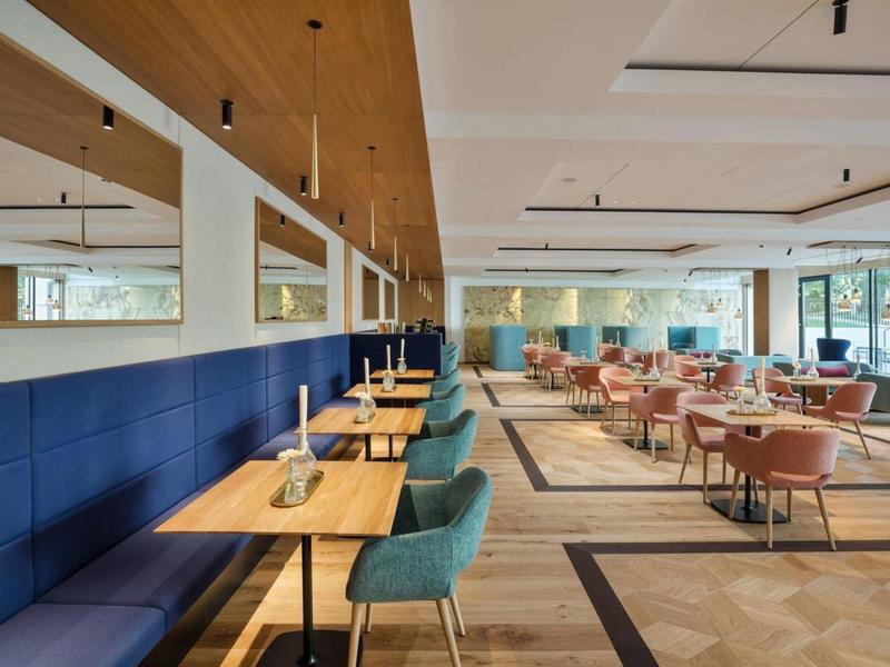 Moderní světlá restaurace s dřevěnou podlahou, modrými lavicemi a pastelovými židlemi.