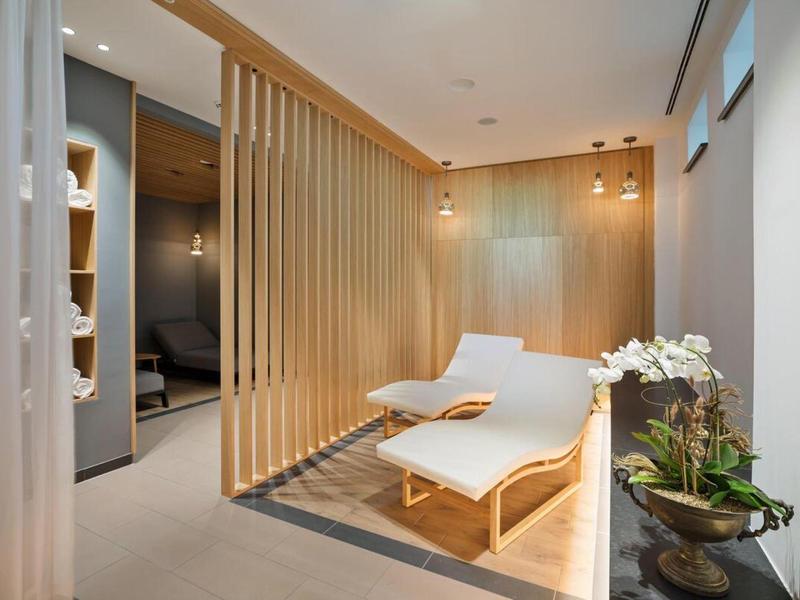 Moderní relaxační místnost se dvěma lehátky, dřevěnou přepážkou a měkkým osvětlením.