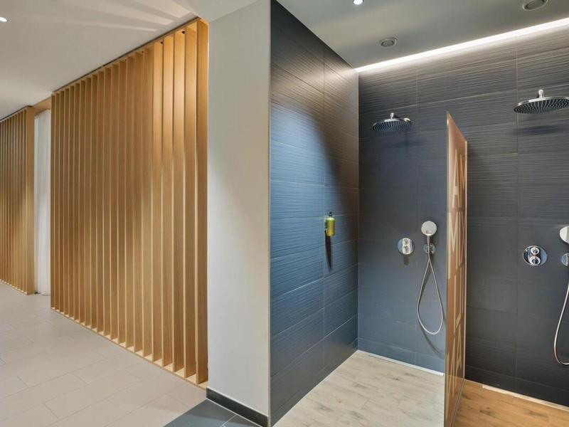 Moderní, elegantní sprchový prostor s béžovými dřevěnými panely a tmavými dlaždicemi v hotelové koupelně.