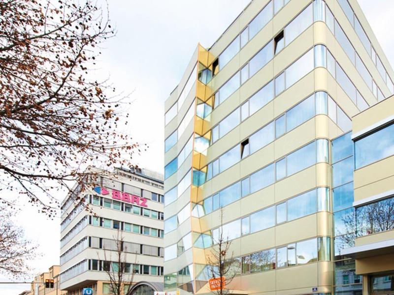 Bâtiments modernes à plusieurs étages avec fenêtres réfléchissantes le long d'une rue urbaine.