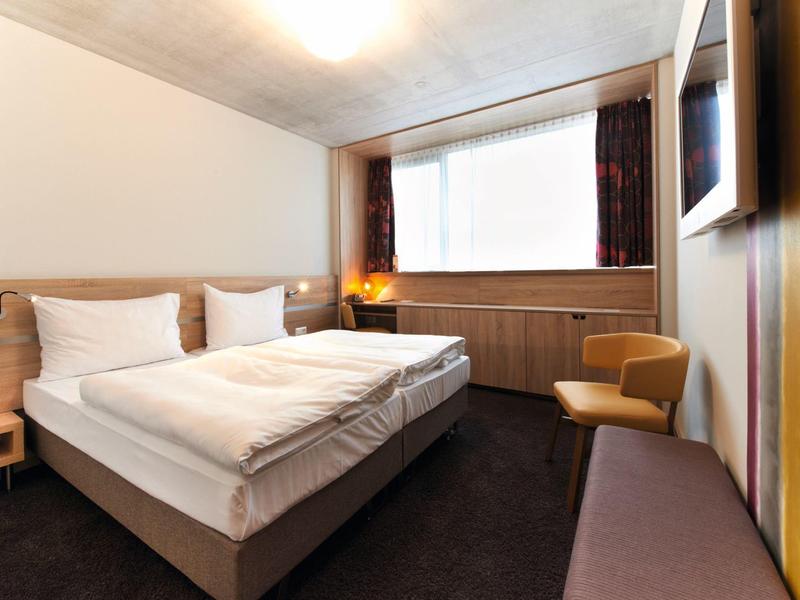 Chambre d'hôtel confortable avec lit double, fenêtre, sièges et TV murale.