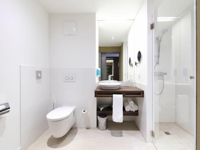 Salle de bain moderne lumineuse avec toilettes blanches, lavabo et douche à l'italienne.