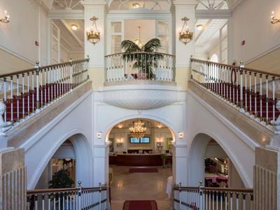 Elegante Hotellobby mit weißem Treppenaufgang und roten Teppichen.
